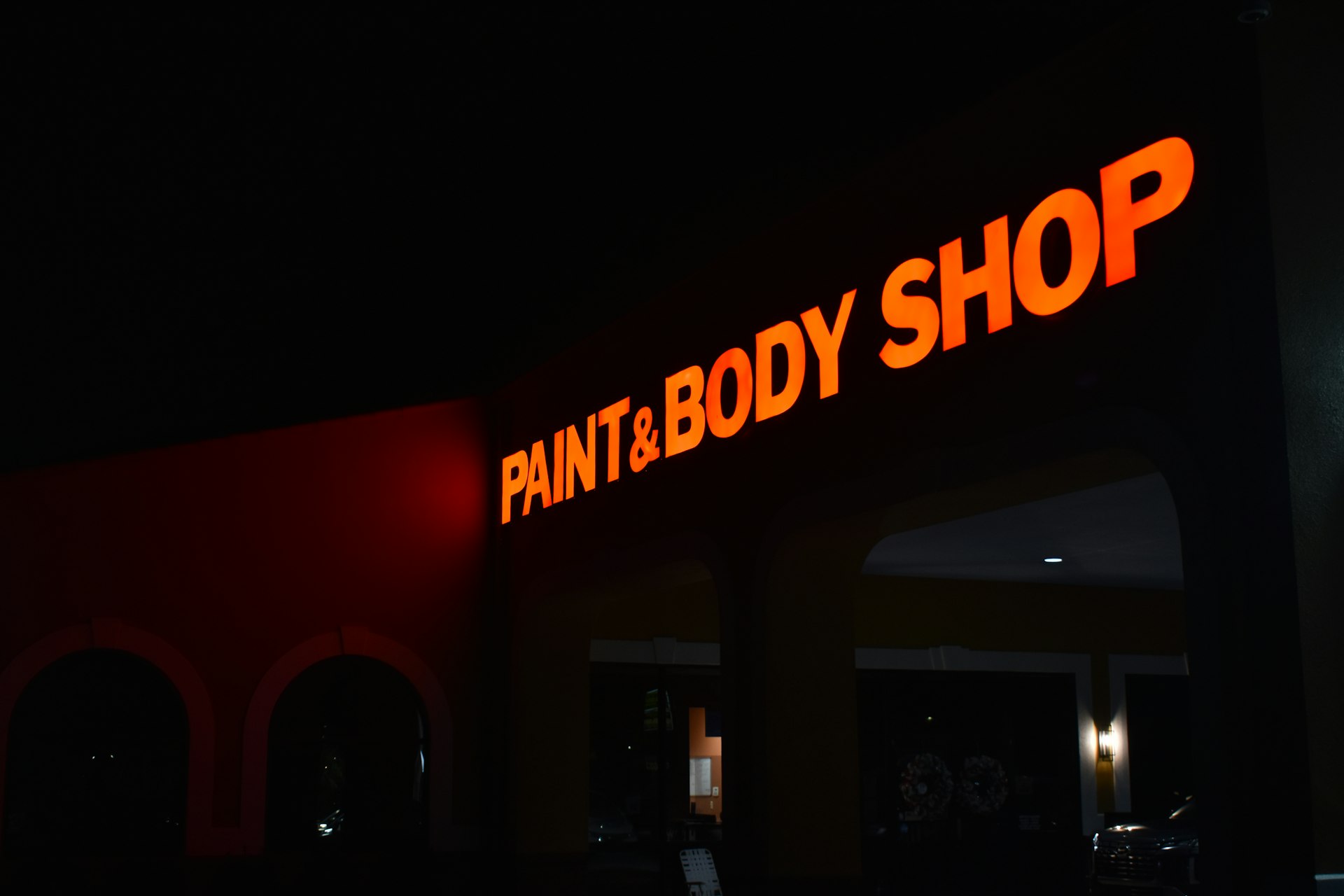 a sign that says paint and body shop lit up at night